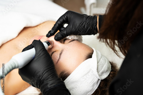 A close-up cosmetologist manipulates a hydropeeling machine to clean and rejuvenate a patient's skin in a modern clinic.