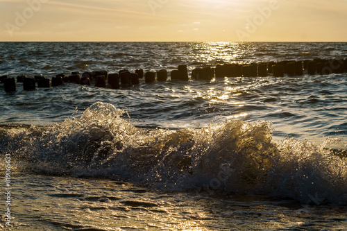 Sunset over the sea. Reflection of sunlight in the sea waves. Breakwater in the sea. The sky in the sunset rays. Baltic Sea.