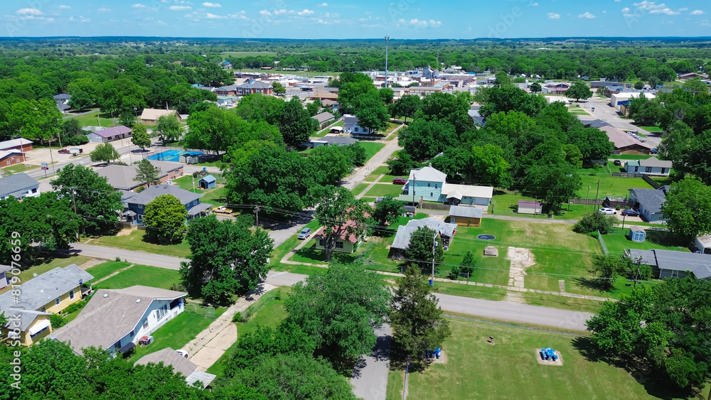 Obraz premium Checotah town of McIntosh County, Oklahoma with suburban residential houses, large backyard, historic downtown Broadway and Main Street background, lush green tree in horizontal line, aerial