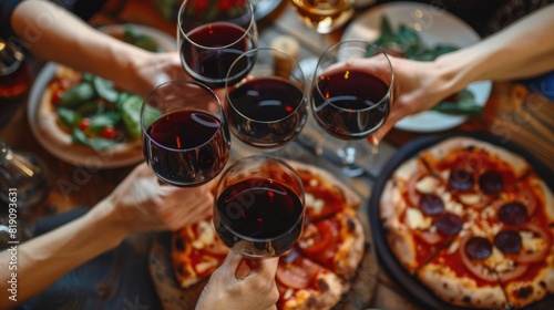 Friends having a pizza party dinner with wine, top view. Group of people clinking glasses of red wine over rustic wooden table of Italian pizza.