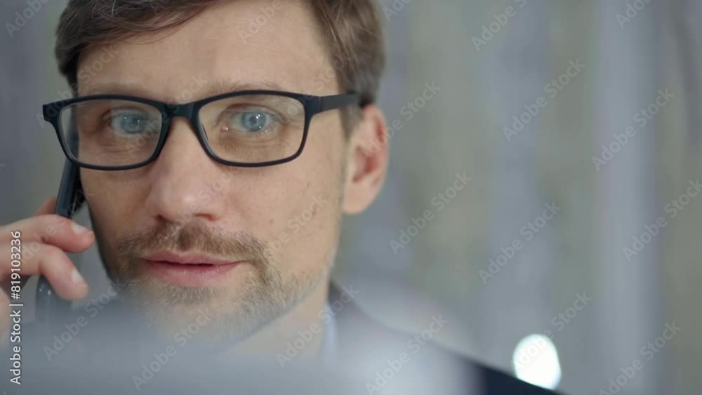 Businessman with glasses speaking on the phone, partially obscured by blurred laptop. Front view and close up portrait Businessman with glasses speaking on the phone, partially obscured by blurred laptop. Front view and close up portrait