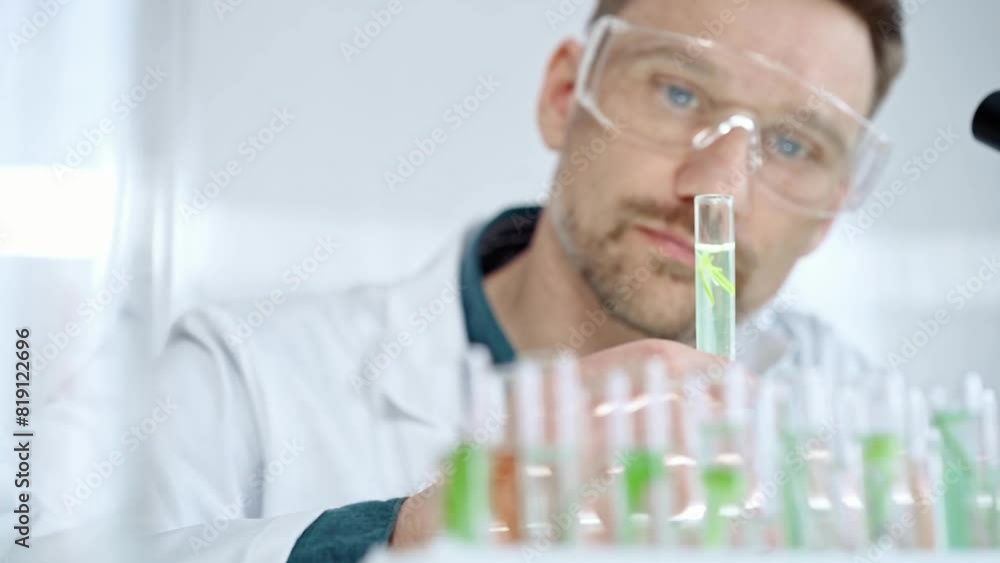 Man researcher with safety glasses is examining lab tube with a green fluid in a modern laboratory, close-up. Science, microbiology and medicine Man researcher with safety glasses is examining lab tube with a green fluid in a modern laboratory, close-up. Science, microbiology and medicine