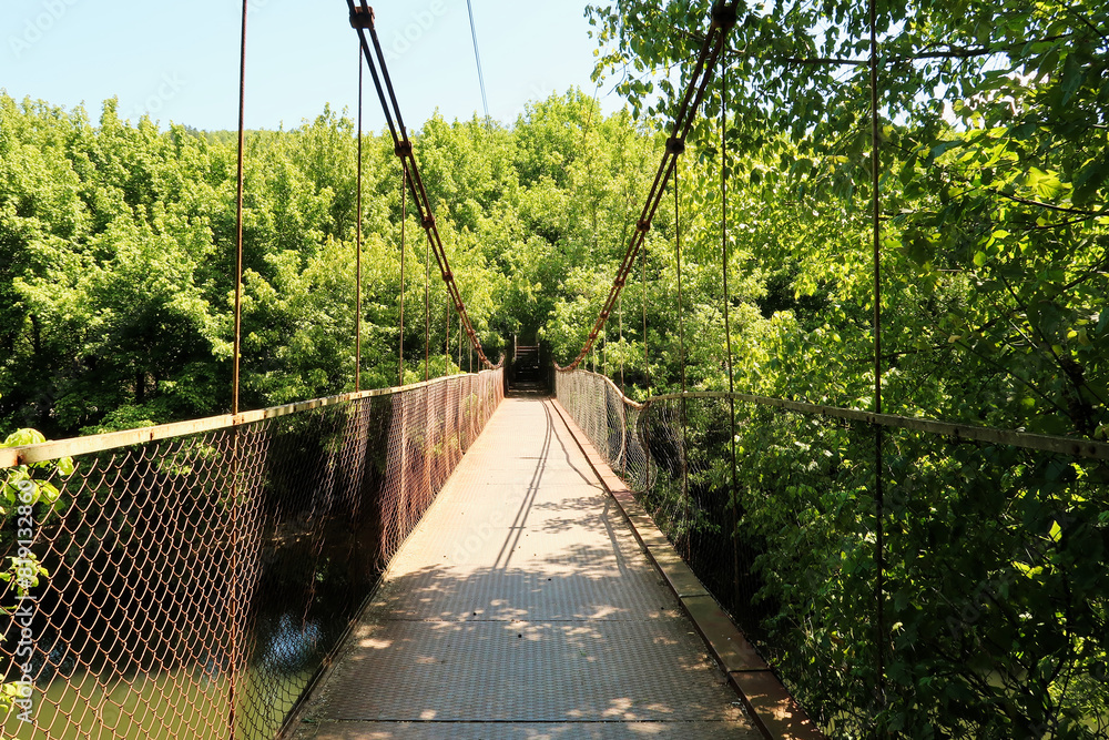 Obraz premium The Mavrikov Rope Bridge, a small metal pedestrian suspension bridge over the Yantra River in a lush dense forest around Veliko Tarnovo, Bulgaria