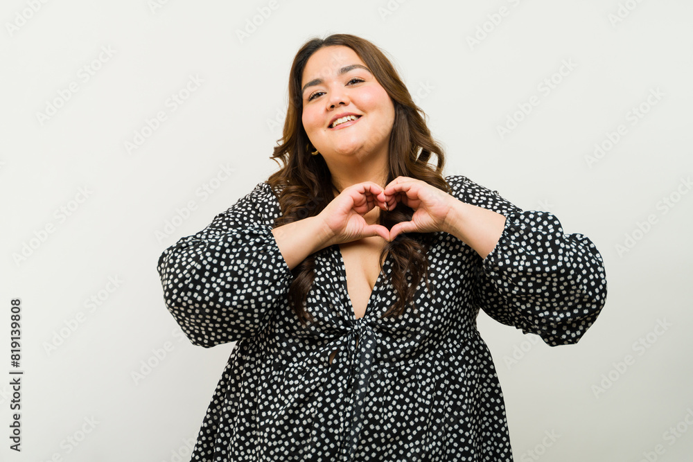 Happy plus-size woman creating a heart shape with her hands against a ...