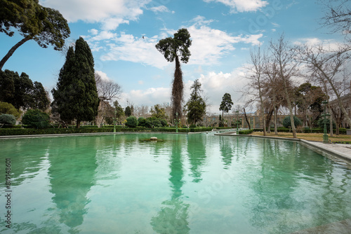 The serene pools of the Golestan Palace are mirrored by towering trees against a cloudy sky. Historic site, Tehran, Iran. photo