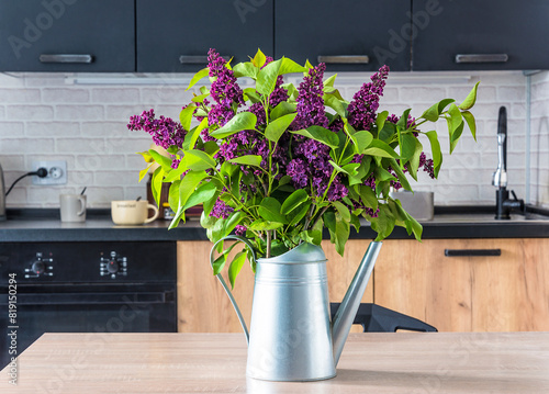 Bunch of purple lilac in watering can on a table in a kitchen