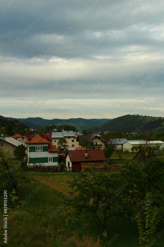A group of houses in a grassy area with trees and hills in the background A group of houses in a grassy area with trees and hills in the background
