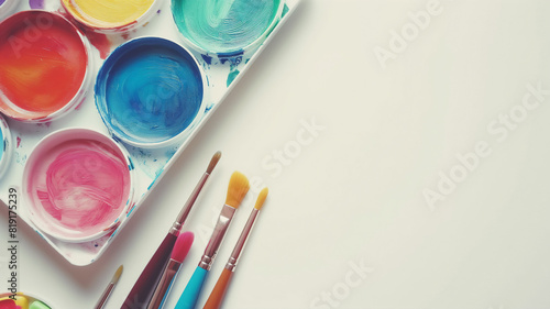 Bright watercolor palette and assorted paintbrushes arranged on a white surface, ready for artistic creativity and painting.