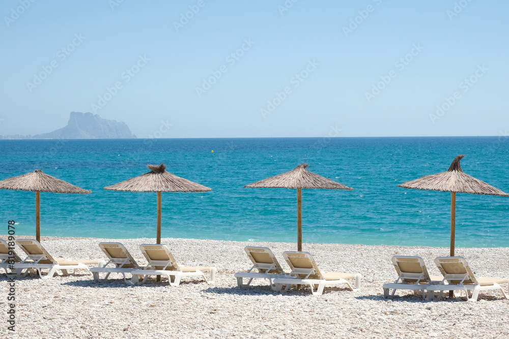 View to turquoise blue Mediterranean Sea and Albir seaside beach in Alicante province, Spain. Raco de Albir Beach with white pebbles, umbrellas and beach sun loungers in beautiful sunny day