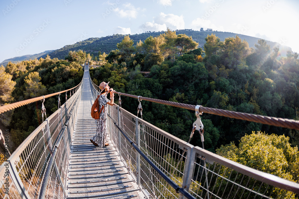 Obraz premium young girl in a hat stands on a suspension bridge and looks dreamily into the distance.
