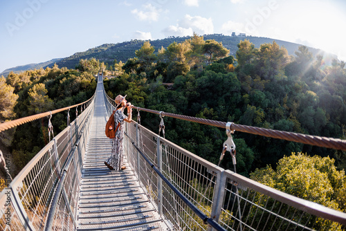 young girl in a hat stands on a suspension bridge and looks dreamily into the distance.