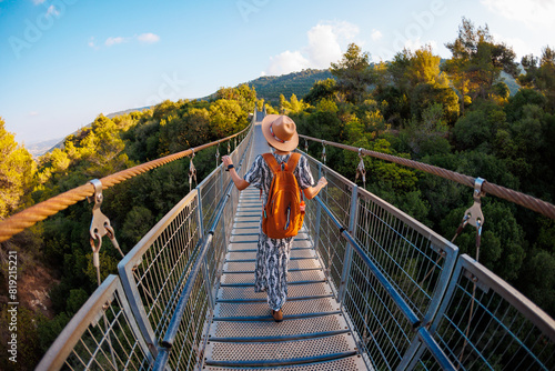 Girl with a backpack. a young woman in a hat and with a backpack walks along a suspension bridge over the river.