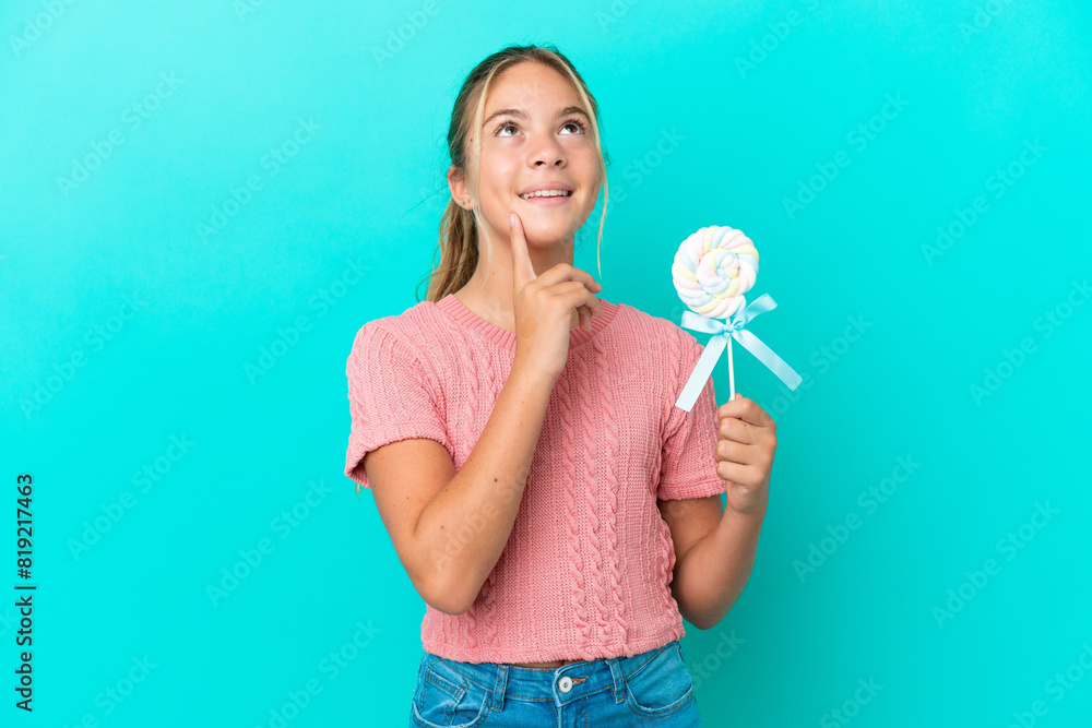 Little Caucasian girl holding a lollipop isolated on blue background thinking an idea while looking up Little Caucasian girl holding a lollipop isolated on blue background thinking an idea while looking up