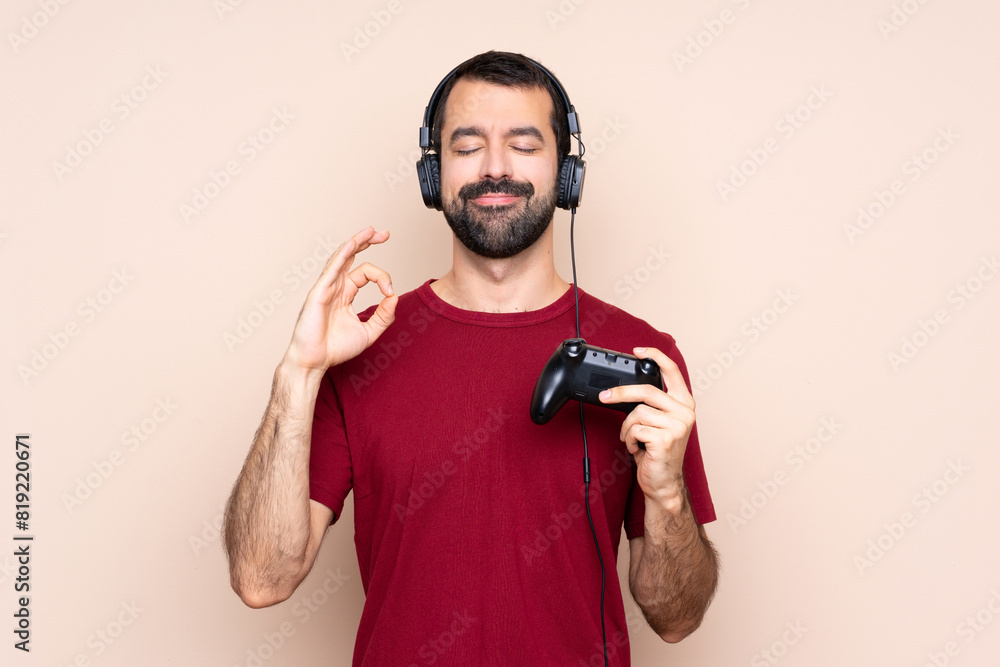 Man playing with a video game controller over isolated wall in zen pose Man playing with a video game controller over isolated wall in zen pose