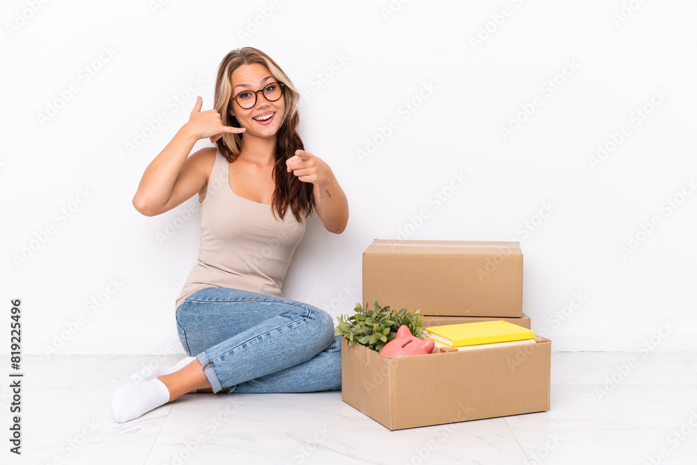 Young Russian girl sitting on the floor isolated on white background making phone gesture and pointing front Young Russian girl sitting on the floor isolated on white background making phone gesture and pointing front