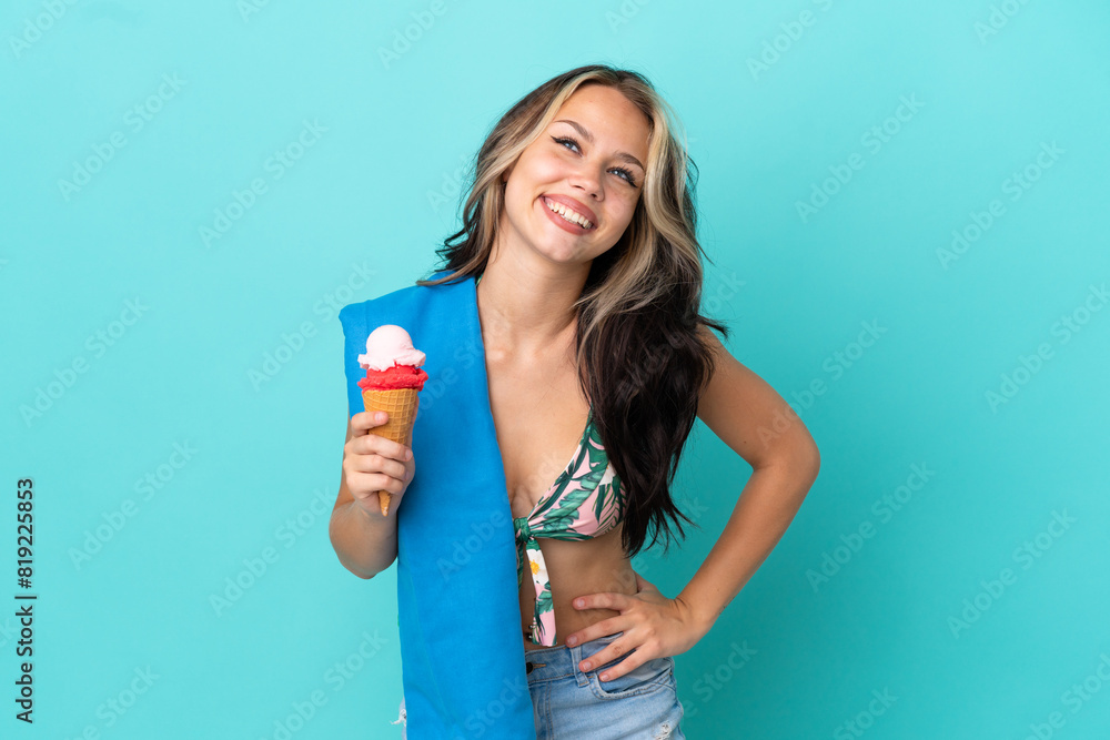 Teenager caucasian girl holding ice cream and towel isolated on blue background posing with arms at hip and smiling Teenager caucasian girl holding ice cream and towel isolated on blue background posing with arms at hip and smiling