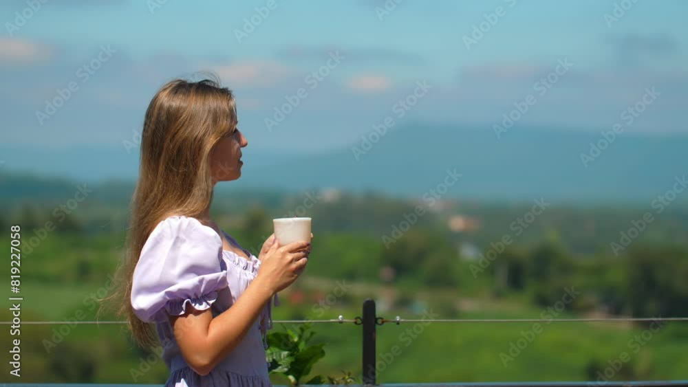 Young woman enjoying peaceful morning with cup of coffee or tea on balcony overlooking scenic landscape with distant mountains and lush greenery. Outdoor relaxation and enjoying nature. Young woman enjoying peaceful morning with cup of coffee or tea on balcony overlooking scenic landscape with distant mountains and lush greenery. Outdoor relaxation and enjoying nature.