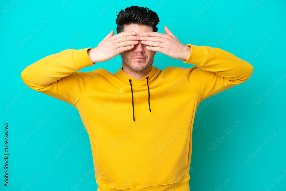 Young caucasian man isolated on blue background covering eyes by hands and smiling Young caucasian man isolated on blue background covering eyes by hands and smiling