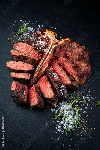 Barbecue dry aged chianina porterhouse beef steak with crystal salt and thyme served as close-up on black design board