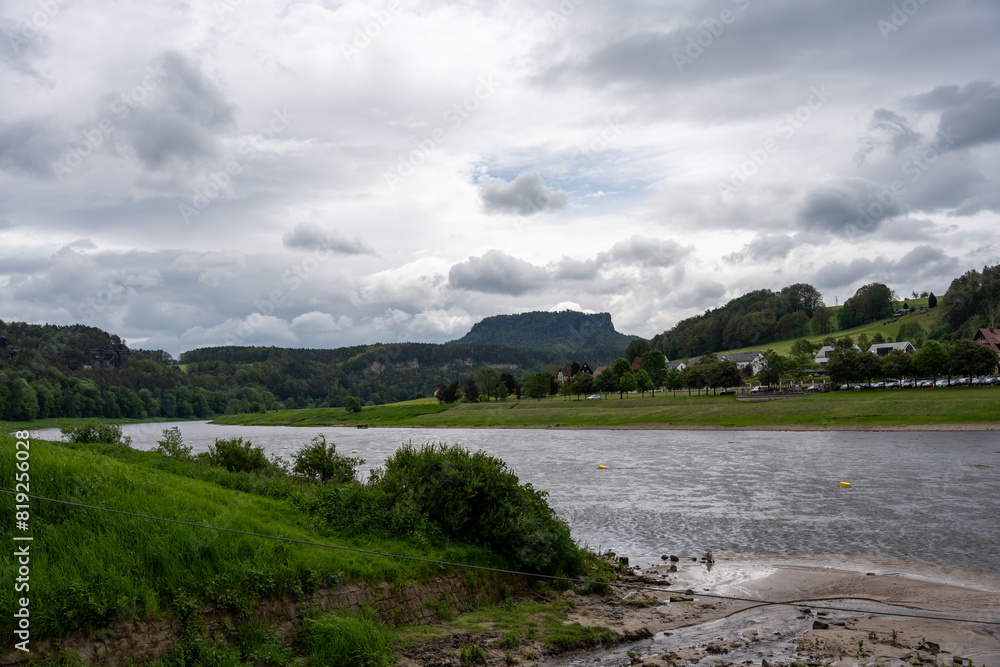 Obraz premium A river with a cloudy sky in the background. The water is calm and the grass is green
