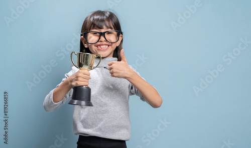 A little girl is holding a gold trophy and is very happy.
