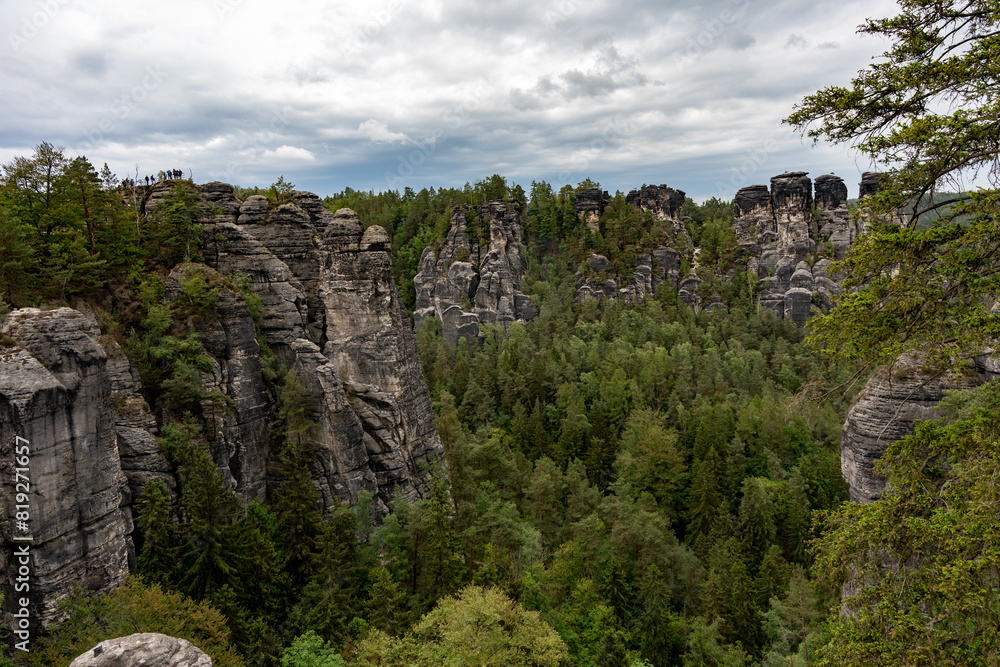 A mountain range with a forest in the background. The sky is cloudy and the trees are green A mountain range with a forest in the background. The sky is cloudy and the trees are green