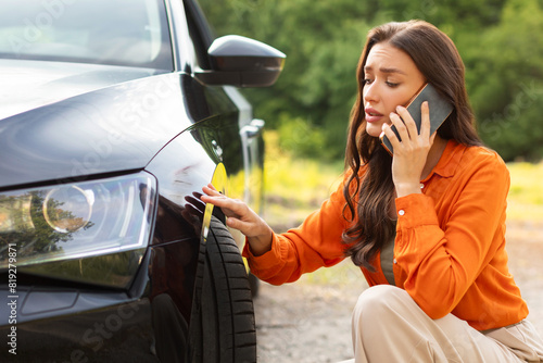 Sad young woman sitting near scratched auto and calling husband for help, having problem with new vehicle © Home-stock