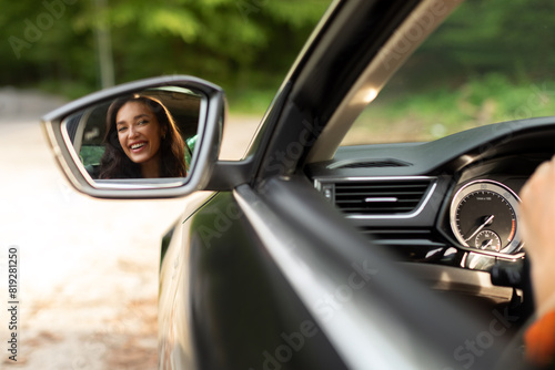 Beautiful young European woman sitting in her new car and looking throw the back view mirror and smiling © Home-stock