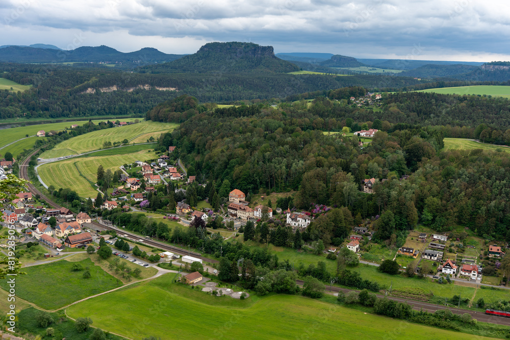 A rural area with a small town and a river. The sky is cloudy and the town is surrounded by green fields A rural area with a small town and a river. The sky is cloudy and the town is surrounded by green fields