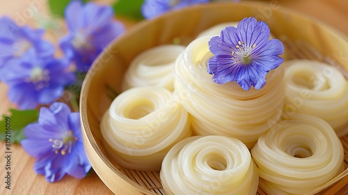   A close-up of a bowl of noodles  featuring a purple flower nestled beside it and an array of blue flowers in the backdrop