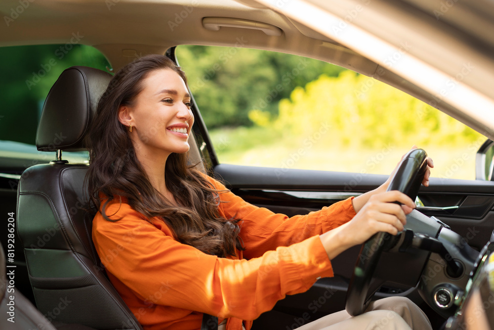 Happy cheerful young woman driver sitting in front seat, holding auto steering wheel, driving her new nice car and smiling