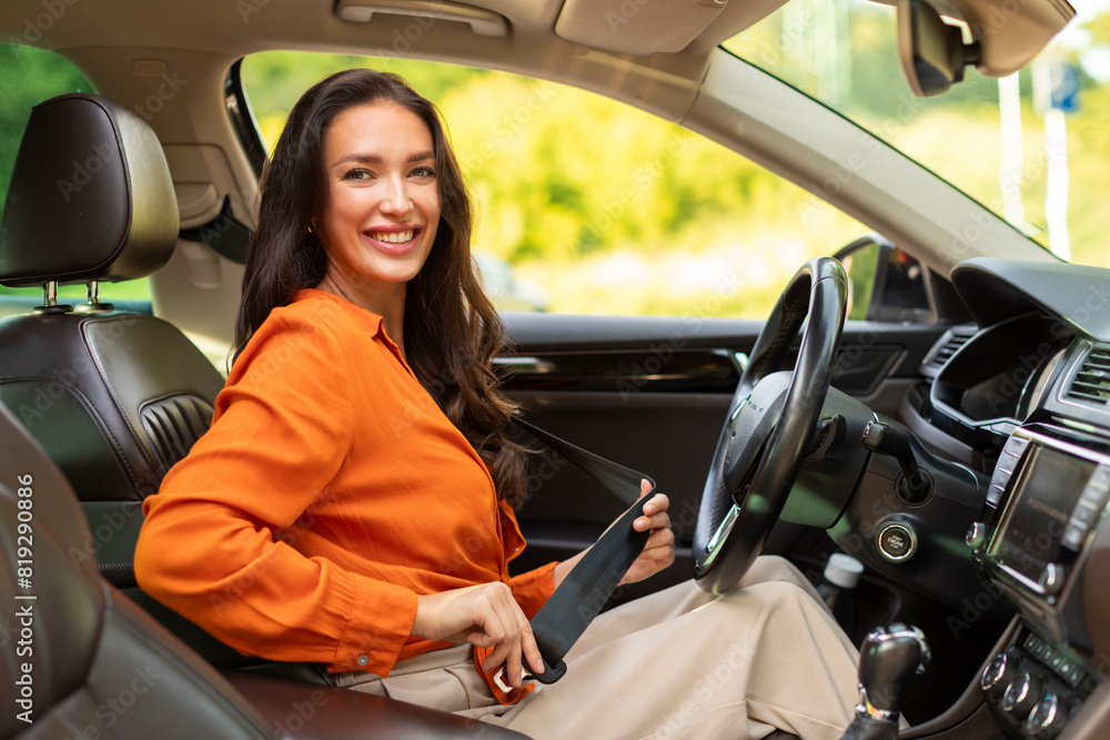 Safety first. Smiling lady fastening seatbelt in her car before driving, following safe ride rules, ready for travel with auto, free space Safety first. Smiling lady fastening seatbelt in her car before driving, following safe ride rules, ready for travel with auto, free space