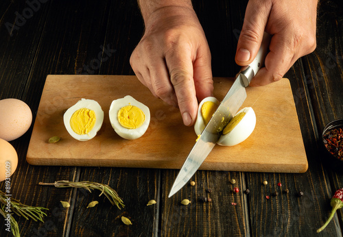 The hands of a chef cut an egg with a knife before preparing a national dish on the kitchen table.