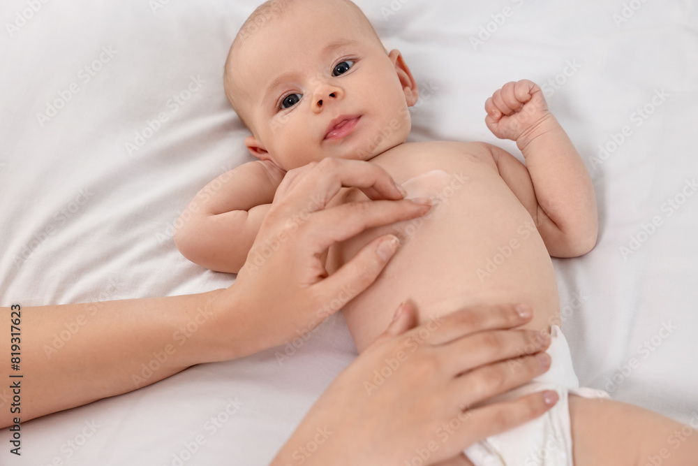 Woman applying body cream onto baby`s skin on bed, closeup Woman applying body cream onto baby`s skin on bed, closeup