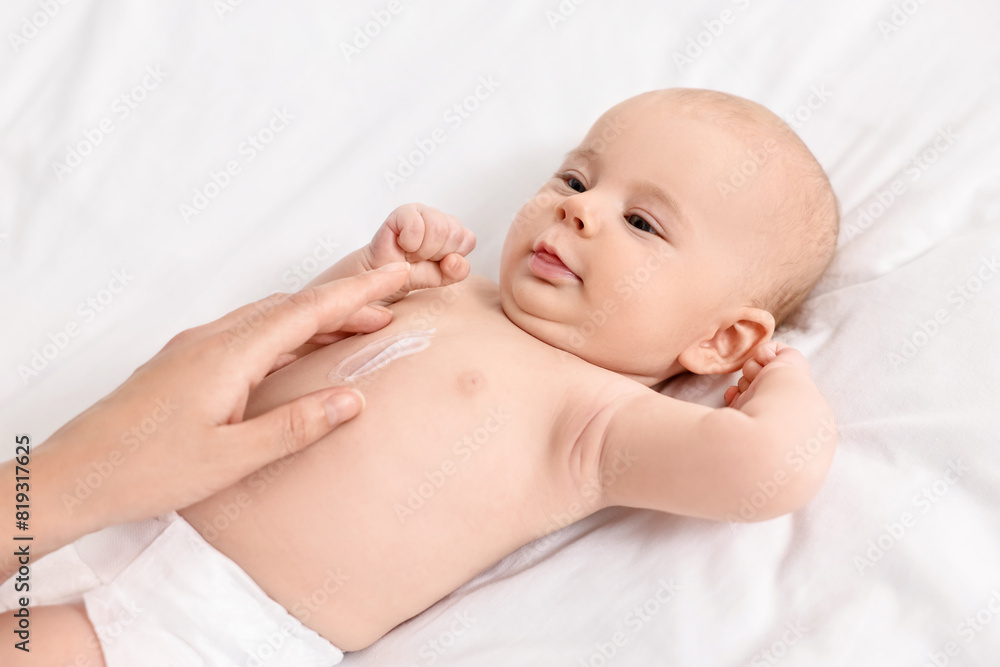 Woman applying body cream onto baby`s skin on bed, closeup Woman applying body cream onto baby`s skin on bed, closeup