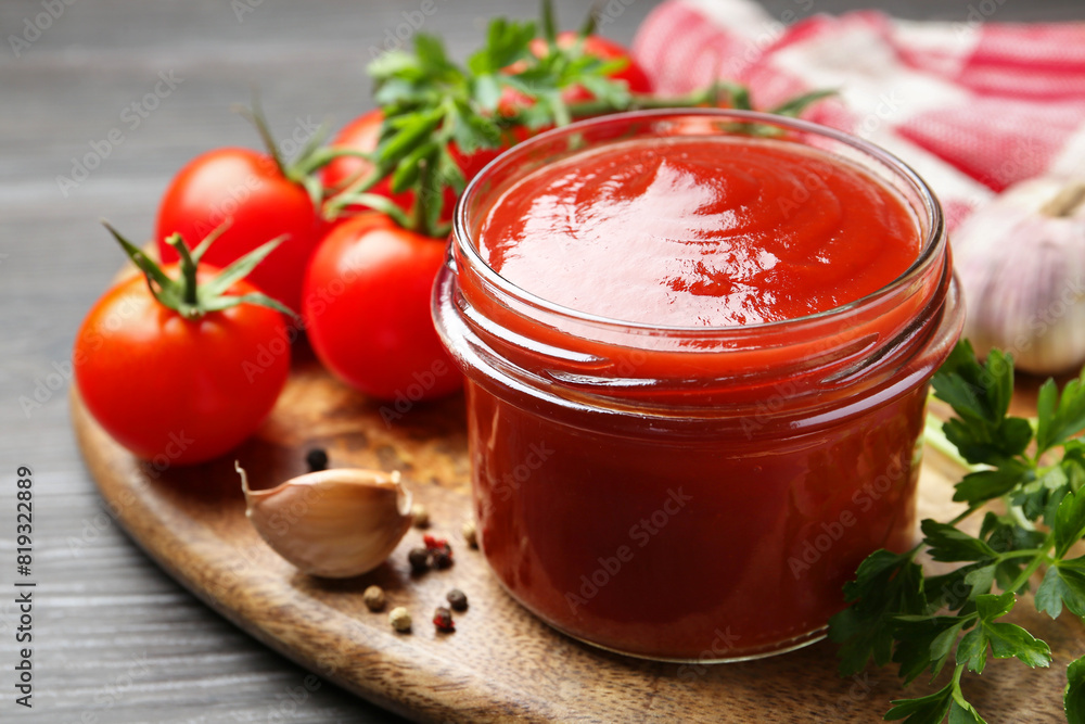 Tasty ketchup, fresh tomatoes, parsley and spices on grey wooden table Tasty ketchup, fresh tomatoes, parsley and spices on grey wooden table