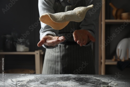 Woman tossing pizza dough at table in kitchen, closeup photo