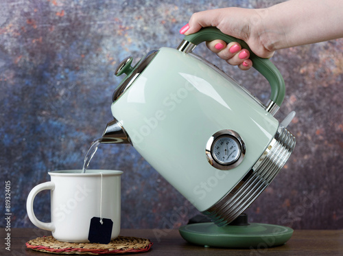 A woman pours hot water from a kettle into a cup with a disposable tea bag.