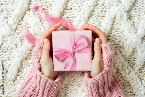 Top view of woman's hands in a sweater holding a pink gift box with a vivid ribbon bow, perfect for Christmas card backgrounds