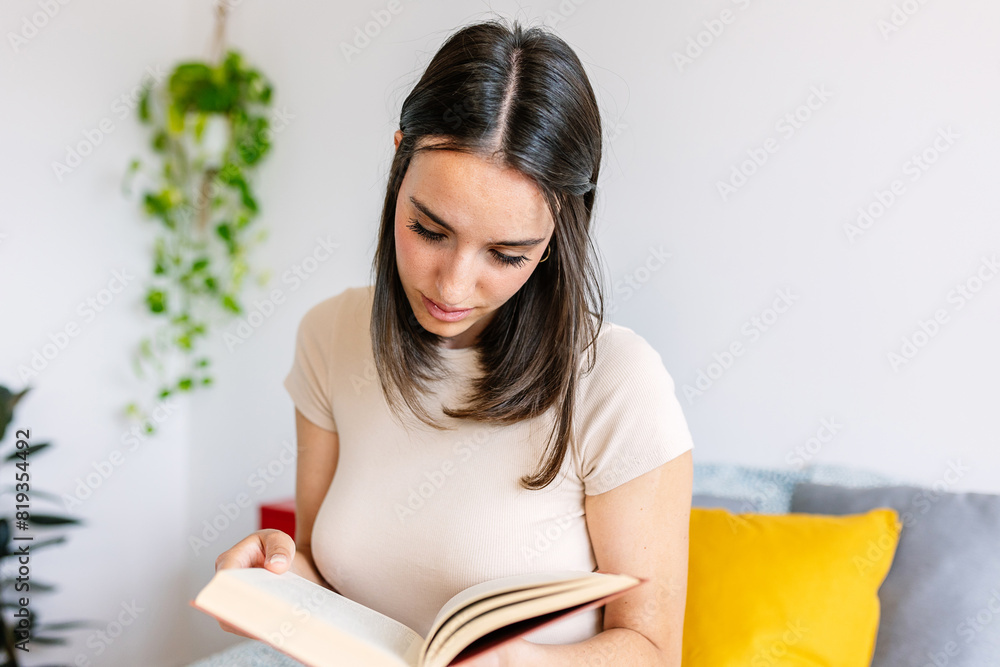 Beautiful caucasian girl reading a book while sitting on bed at home. Leisure activity concept. Beautiful caucasian girl reading a book while sitting on bed at home. Leisure activity concept.