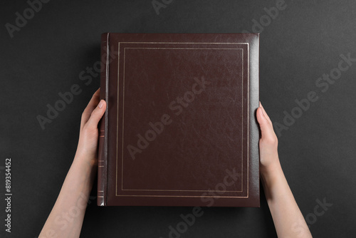 Woman with photo album at black table, top view