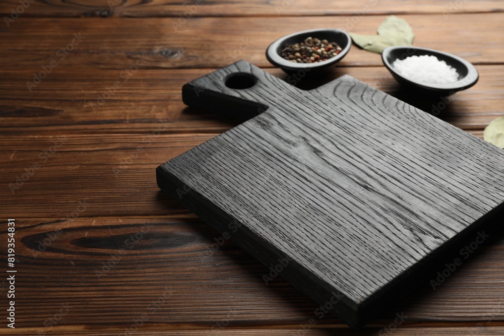 Black cutting board, salt, pepper and bay leaves on wooden table. Space for text Black cutting board, salt, pepper and bay leaves on wooden table. Space for text