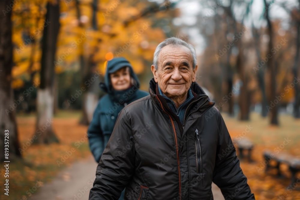 Content senior man enjoys a peaceful walk in an autumn park with a woman in the background Content senior man enjoys a peaceful walk in an autumn park with a woman in the background