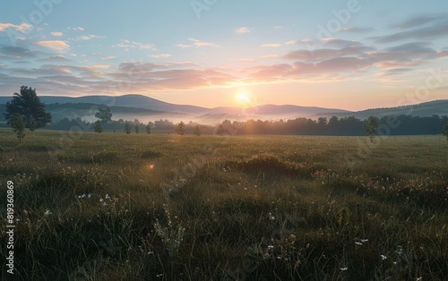 Sunrise over a serene field with distant mountains and scattered trees.