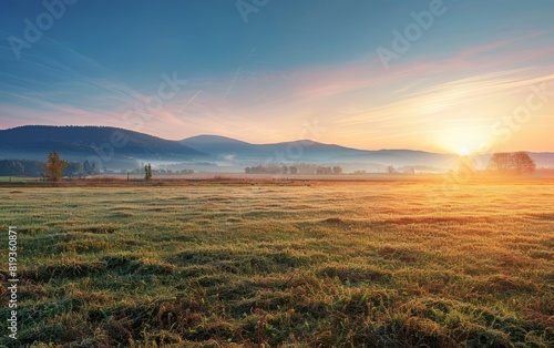 Sunrise over a serene field with distant mountains and scattered trees.