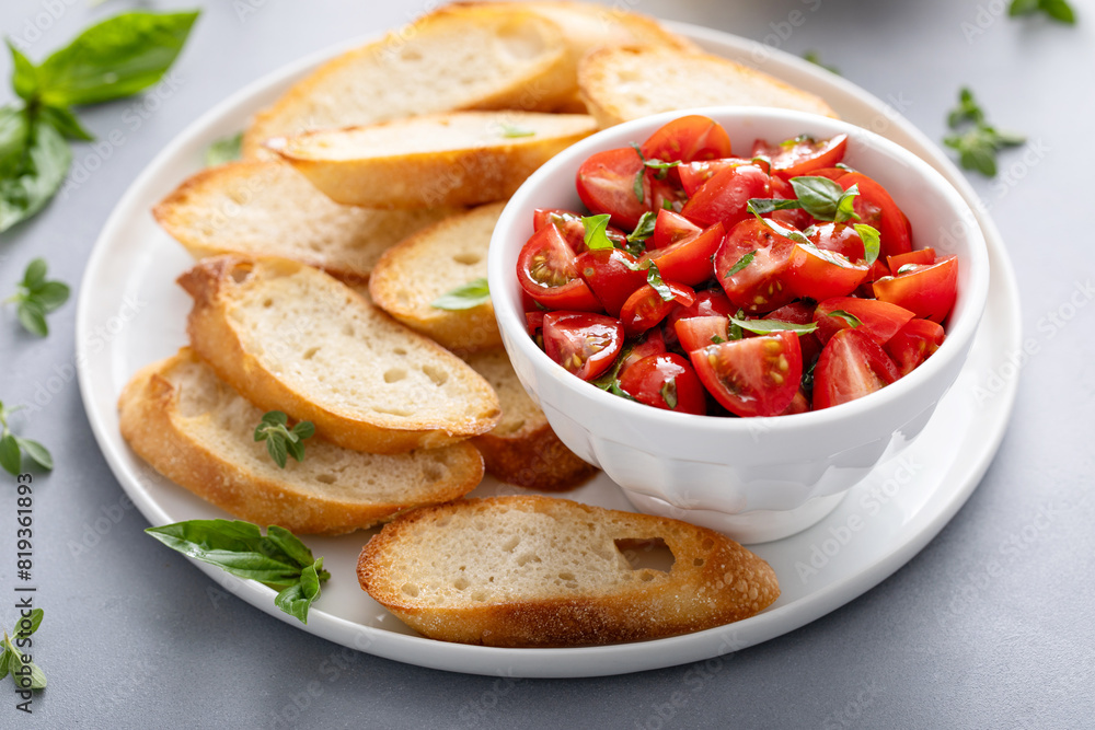 Ripe tomatoes with basil in a bowl beside sliced toasted baguette Ripe tomatoes with basil in a bowl beside sliced toasted baguette