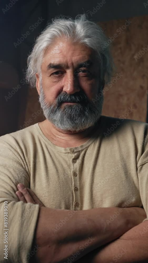 Strong engineer with grey beard stands with crossed arms after difficult work at making aircraft in garage. Aged man looks with satisfied and concerned expression Vertical Shot. Strong engineer with grey beard stands with crossed arms after difficult work at making aircraft in garage. Aged man looks with satisfied and concerned expression Vertical Shot.