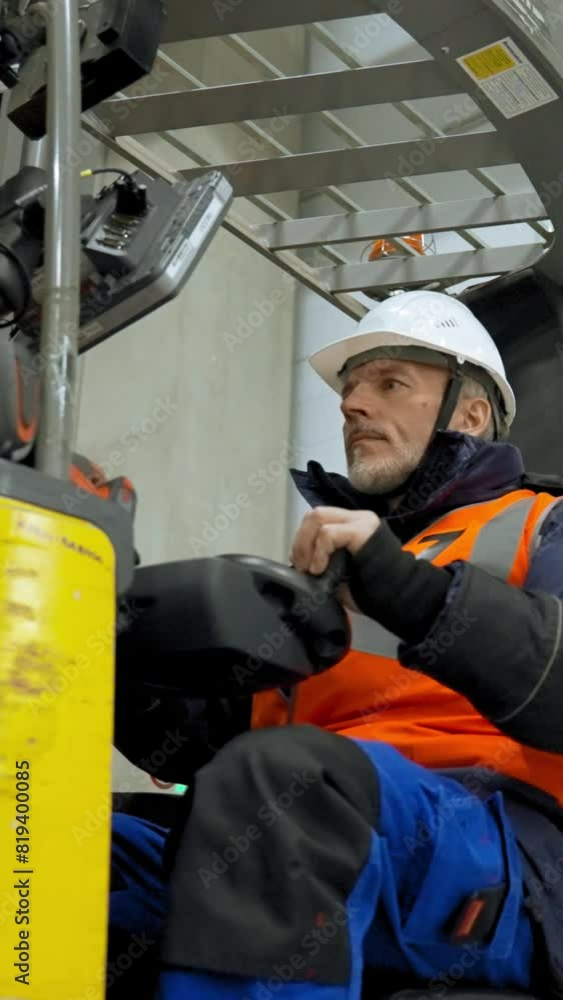 Engineer controls forklift truck pushing buttons on monitor. Bearded man sits in cabin of machine in storage terminal low angle shot slow motion Vertical Shot.