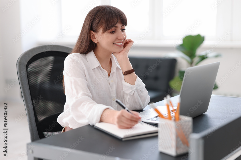 Woman taking notes during webinar at table indoors Woman taking notes during webinar at table indoors