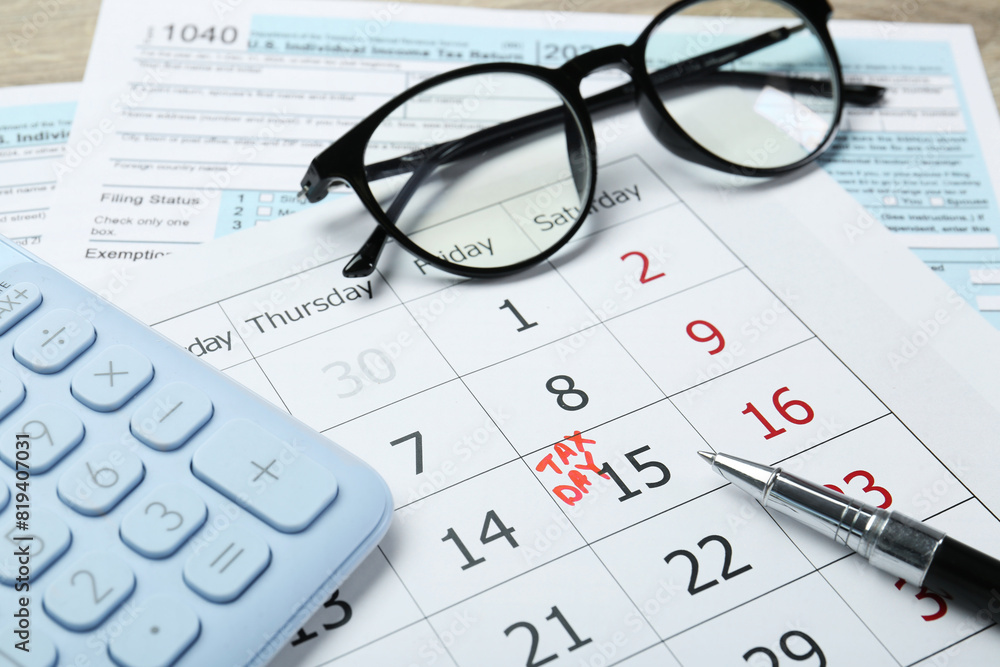 Tax day. Calendar with date reminder, documents, pen, glasses and calculator on table Tax day. Calendar with date reminder, documents, pen, glasses and calculator on table